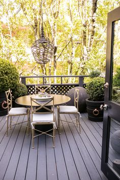 a table and chairs on a wooden deck with potted trees in the back ground