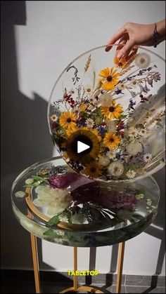 a person is arranging flowers in a glass bowl on a table with a gold stand