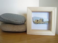 two rocks are sitting next to a wooden frame with a small painting on top of it