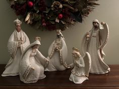 three figurines sitting on top of a wooden table next to a christmas wreath