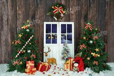 two christmas trees and presents in front of a wooden door with snow on the ground