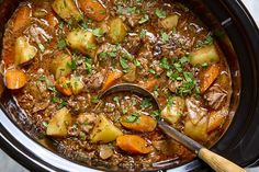 a crock pot filled with beef stew and potatoes, garnished with parsley