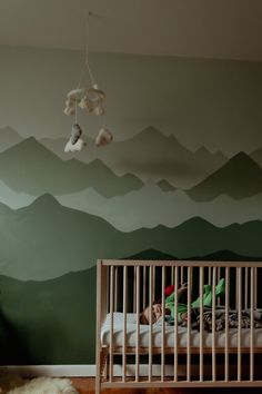 a child's room with mountains painted on the wall and a crib in front