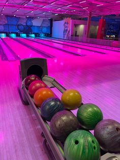 several bowling balls are lined up in a row on a bowling alley with pink lighting