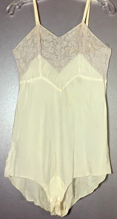 This is one pretty vintage 1940s teddy. The teddy is an off white, cream color with a just barely lavender lace trim. There are adjustable straps and the hardware is still there and it works fine. There are 2 buttons at the crotch. The label on the inside says LadyLove 36.  There is a tiny faint black mark by the base of one of the straps and there is a water stain but so faint it is hard to see. If you look closely at the lower center part there is a very faint stain, the crotch is ok. Buttons are there. On the back lower right near the bottom is a tiny, tiny pin hole.  All the flaws are pictured.  Measurements for this beautiful vintage 1940s teddy are: From the center front "V" to the center of the front crotch flap is 25.5" long. The bust is 35". The waist is 32". Free Shipping in the Vintage Sheer Sleeveless Camisole, Beige Camisole For Daywear, Cream Lace Camisole For Daywear, Vintage Sheer Camisole For Summer, Vintage Cream Lace Top For Summer, Vintage Delicate Lace Camisole For Daywear, Cream Lace Trim Camisole For Daywear, Beige Lace Trim Camisole For Daywear, Feminine Cream Lace Camisole