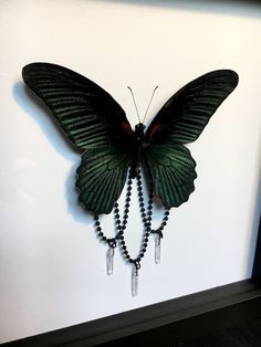 a green butterfly hanging from the side of a wall next to a black beaded necklace