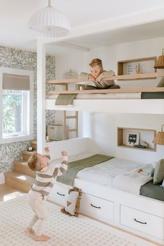 a young child standing on the bottom bunk of a bed in a room with green and white wallpaper