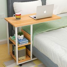 a laptop computer sitting on top of a wooden table next to a bed with white sheets