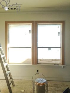 an empty room with two windows and a ladder in the foreground that has been painted white