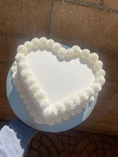 a white heart shaped cake sitting on top of a blue plate next to a brick wall