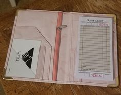 a pink binder sitting on top of a wooden table next to a pen and paper