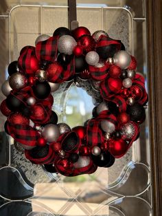 a red and black christmas wreath hanging on a glass door with ornaments in the shape of balls