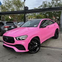 a bright pink mercedes gle is parked in front of a black bmw dealership