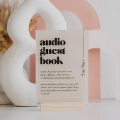 a book sitting on top of a table next to a white vase with flowers in it