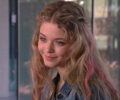 a woman with long blonde hair wearing a denim shirt and jeans jacket smiling at the camera