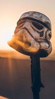 a close up of a star wars helmet on a pole with the sun in the background