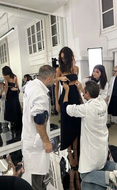 a group of people standing in front of a mirror while one person adjusts the dress