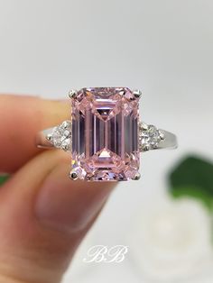 a person holding a pink diamond ring in their hand with the center stone surrounded by three diamonds