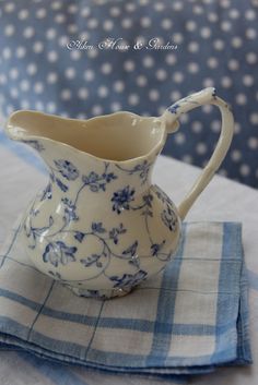 a blue and white flowered pitcher sitting on top of a table cloth next to a napkin