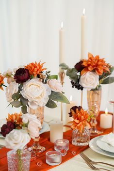 an arrangement of flowers in vases on a table with other place settings and candles