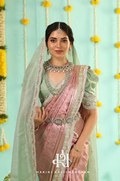 a woman in a pink and green sari posing for a photo with flowers on the wall behind her