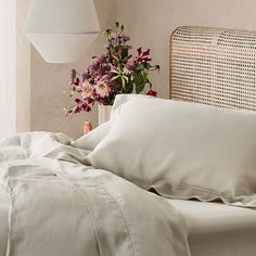 a bed with pink sheets and pillows next to a vase filled with flowers on top of it