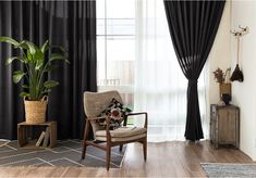 a living room with black drapes and a chair next to a plant in the corner