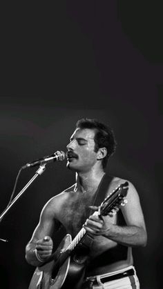 a shirtless man holding a guitar and singing into a microphone