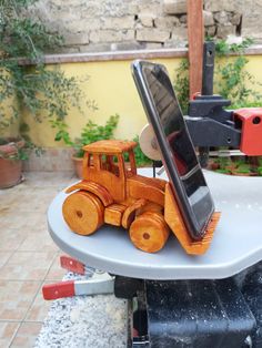 a cell phone sitting on top of a wooden toy bulldozer in the shape of a tractor