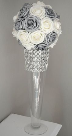 a vase filled with white and grey flowers on top of a wooden table next to a wall