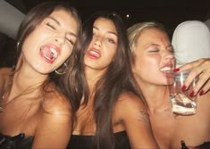 three beautiful young women sitting next to each other holding drinks in their hands and laughing