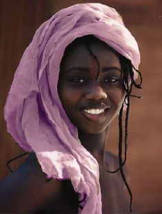 a woman with dreadlocks and a pink scarf on her head smiles at the camera