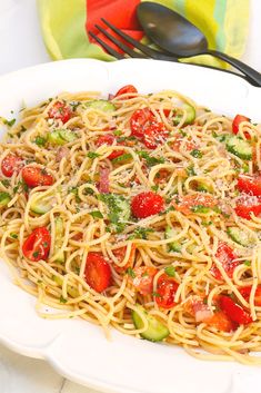 a plate of pasta with tomatoes and zucchini on it next to a fork