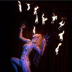 a woman with fire sticks in her hands and body painted blue, white and pink