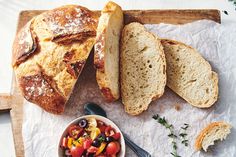 an assortment of breads and vegetables on a cutting board next to a bowl of salad