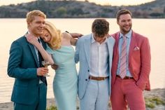 three men and a woman standing next to each other in front of a body of water