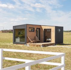 a tiny house sitting on top of a grass covered field next to a white fence