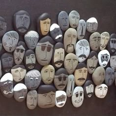 some rocks with faces painted on them sitting next to each other in the shape of people's heads