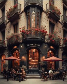 people sitting at tables in front of a coffee shop with red flowers on the balconies