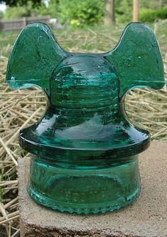 a green glass vase sitting on top of a cement block in front of some grass