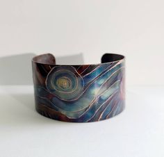 "This unique copper bracelet is made by painting patterns onto copper with a torch, and as the copper heats and cools it turns different colors naturally! Its quite an amazing process! Ive then engraved high lights into the pattern which makes it pop! Such a fun and whimsical design! The cuff is 1\" wide and is flexible enough so that you can make it fit your wrist. It is protected with a sealant to keep it from further oxidizing. These are custom made per order, so please keep in mind that with Bohemian Electroformed Cuff Bracelet Bangle, Handmade Artistic Copper Bracelets, Wearable Art Copper Bangle Bracelets, Handmade Artistic Copper Bracelet, Artistic Patina Cuff Bracelet As Gift, Artistic Patina Cuff Bracelet Gift, Artistic Patina Bangle Bracelet, Copper Bangle Bracelets In Wearable Art Style, Bronze Wearable Art Cuff Bracelet As Gift