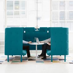 two people sitting at a table with laptops in front of them, both on separate blue chairs