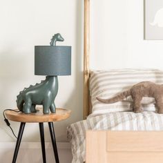 a toy dinosaur on a table next to a bed with a pillow and lamp in the corner