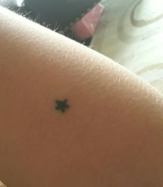 a small black star tattoo on the back of a woman's left arm,