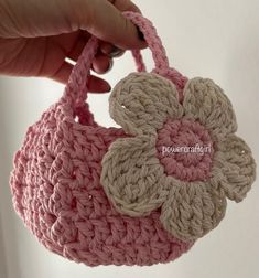 a crocheted pink purse with a flower on the front and side, held up by a woman's hand