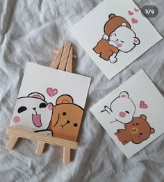 three small paintings of bears on white paper with wooden easel and paintbrushes