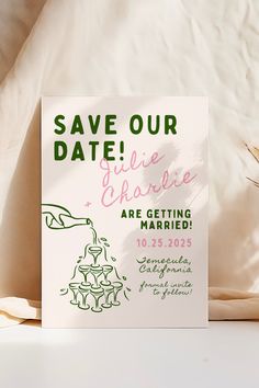 a save the date card sitting on top of a bed next to a vase with flowers