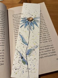 an open book with watercolors on it and a blue flower in the middle