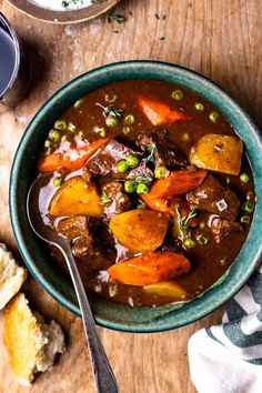 a bowl of beef stew with carrots, peas and bread on a wooden table