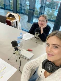 two women are sitting at a table with headphones on and one is listening to the microphone